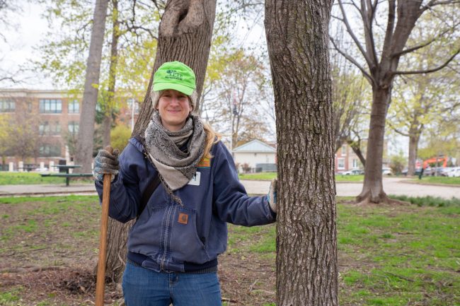A volunteer tree planter smiling next to a mature tree in Philadelphia