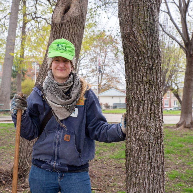 A volunteer tree planter smiling next to a mature tree in Philadelphia