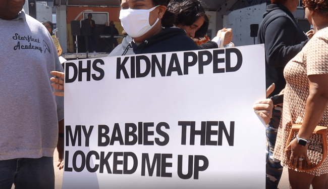Protesters carry a sign at a May 2022 protest at LOVE Park after City Council released a scathing reports on the Department of Human Services’ lapses in caring for children. (Josh Childs)