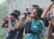 A picture of students at Lankenau Environmental Science Magnet High School look through binoculars during a learning activity outside the school building.