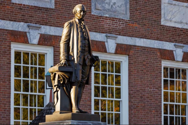 A statue of George Washington stands in front of Independence Hall as the sun rises over Philadelphia.