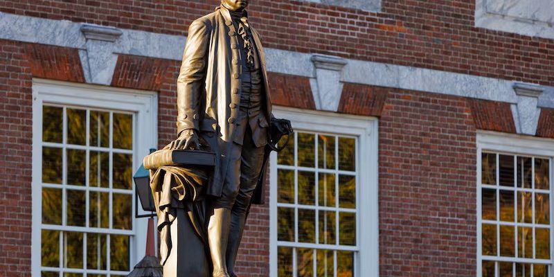 A statue of George Washington stands in front of Independence Hall as the sun rises over Philadelphia.